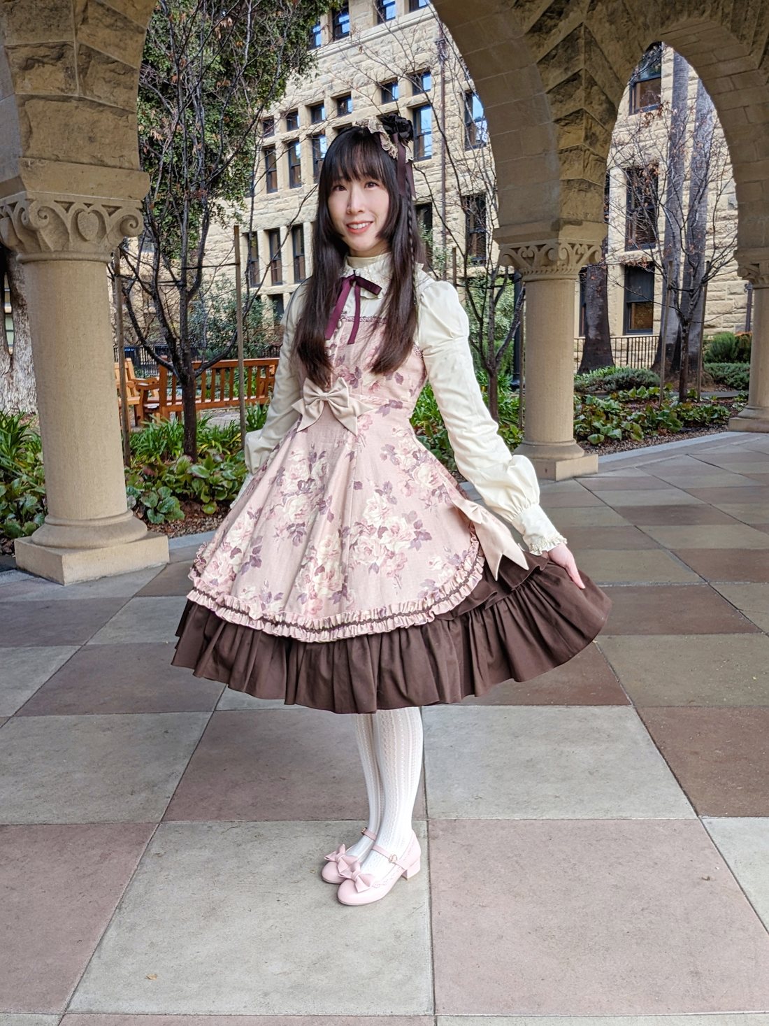 kayas.coords wearing a pink floral jumperskirt with brown ruffled hem in a sunlit courtyard